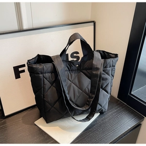 Detail of black quilted nylon tote bag showing oversized diamond pattern and metal clasp