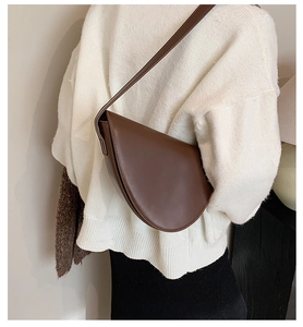 Borsa a sella marrone minimalista indossata da modella con maglione bianco