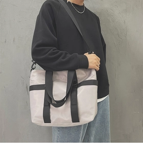 Detailed view of grey nylon tote bag with black wide strap on model with minimalist wall