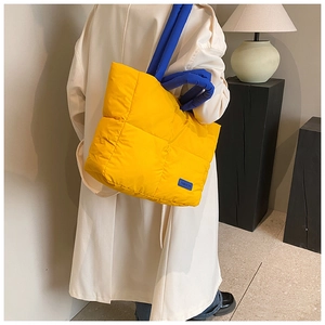 Sac fourre-tout matelassé jaune avec anses bleues contrastées porté par un mannequin