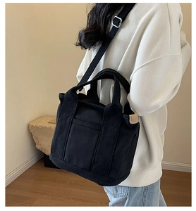 Detail of minimalist black canvas crossbody bag with wide handle and side leather tag