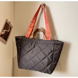 Detail of quilted nylon tote bag with contrasting orange straps and metallic snap closure