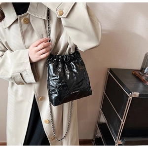 Detail of glossy quilted bucket bag with silver metal logo and chain strap