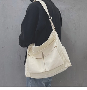 Dettaglio di una borsa a tracolla in tela beige con doppie tasche frontali su una modella