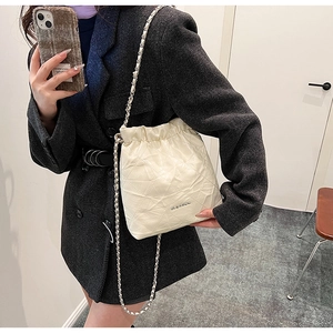 Detail of off-white bucket bag featuring quilted diamond pattern and silver chain strap