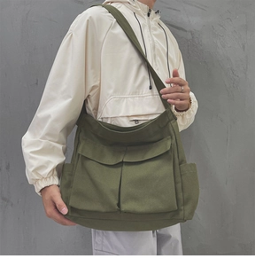 Dettaglio della borsa a tracolla in tela verde militare con ampie tasche anteriori a patta