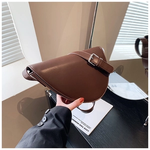 Dettaglio di una borsa a sella in pelle marrone scuro tenuta in mano su legno