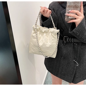Quilted cream bucket bag featuring drawstring closure and metal chain strap on model