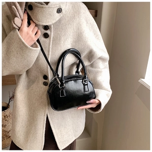 Close-up of a black patent leather mini shell handbag shown with a beige coat