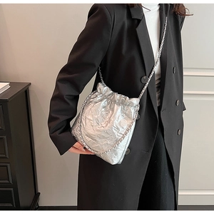 Silver metallic pleated bucket bag with drawstring and chain strap on black coat