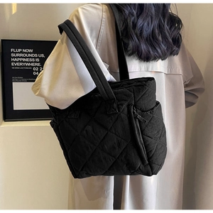 Detail of black quilted nylon tote bag showing diamond stitching and side zipper design