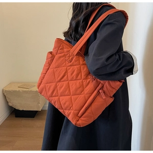 Detail of an orange quilted puffer tote bag with diamond stitching and wide shoulder strap