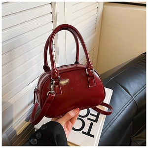 Detail of a dark red patent leather handbag with dual handles and a metallic zipper
