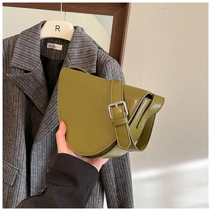 Dettaglio di una borsa a sella in pelle verde erba tenuta su un cappotto di lana grigio