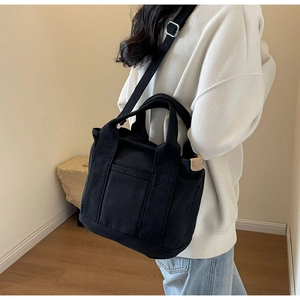 Detail of black canvas tote bag showing adjustable strap and spacious front pocket