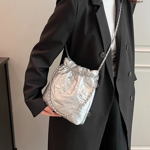 Silver quilted drawstring bucket bag with chain strap shown on model in studio setting