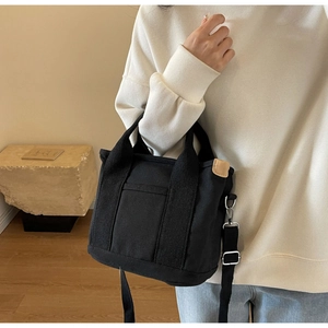 Detail of black canvas tote bag showing the side leather tag and adjustable strap