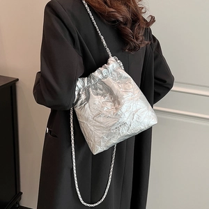 Quilted silver metallic bucket bag with chain strap worn by a model in a black suit