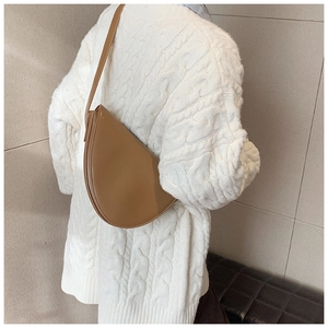 Vista dettagliata di una borsa a mezzaluna color cuoio indossata su un maglione bianco