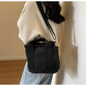 Close-up of black canvas tote bag showing the textured webbing handle and side leather trim
