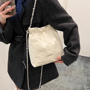 Chic white quilted drawstring bucket bag with silver chain strap shown on a model