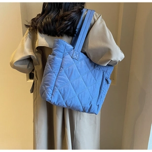 Detailed view of the bright blue quilted nylon tote bag worn with a khaki coat