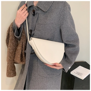 Dettaglio di una borsa a tracolla bianca a mezzaluna indossata con un cappotto di lana grigio