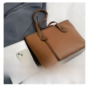 Detail showing brown lychee grain leather tote bag capacity with iPad and phone