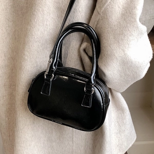 Elegant black patent leather crossbody handbag with circular handles on wool coat