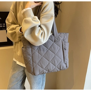 Detail of grey quilted nylon tote bag with zipper pockets worn on shoulder by a model