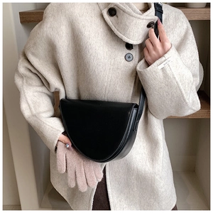 Primo piano della borsa a tracolla a mezzaluna in pelle nera minimalista indossata con un cappotto