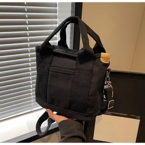 Detail view of black canvas tote bag showing wide handles and adjustable strap buckle