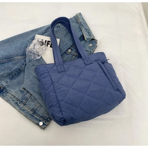 Detail of dark blue quilted nylon tote bag featuring diamond pattern on a white background