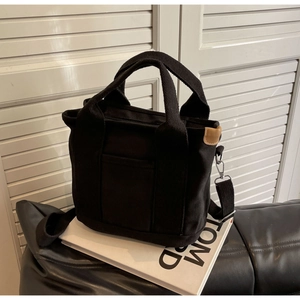 Detail of a black canvas tote bag with brown leather trim and adjustable shoulder strap
