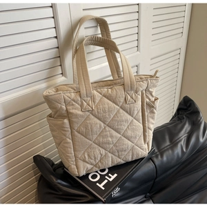 Detail of beige quilted nylon tote bag featuring side pockets and a sturdy zipper closure