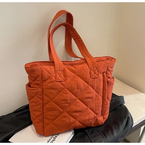 Detail of quilted nylon tote bag in brick red showing side pockets and padded texture