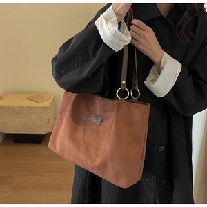 Detail of brown suede tote bag with rhombus texture and gold metal ring strap attachments
