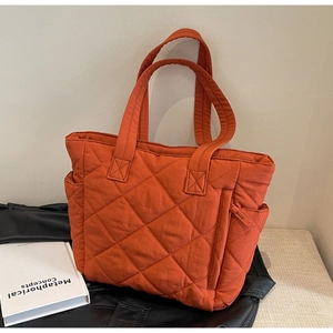Detail of quilted orange nylon tote bag showing zipper pockets and diamond stitch texture
