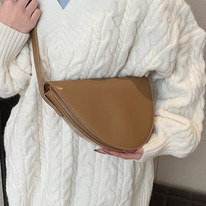 Borsa a tracolla a mezzaluna in pelle marrone chiaro indossata su un maglione bianco