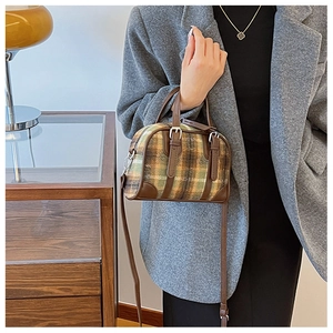 Detail of Boston bag with green plaid fabric and brown leather straps in home setting