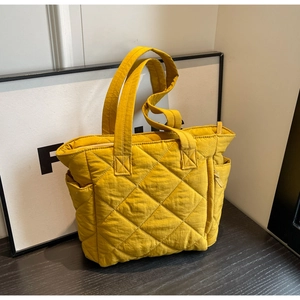 Detail of ginger yellow quilted nylon tote bag featuring side pocket and diamond pattern