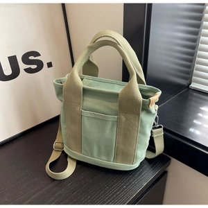 Detail of light green canvas bag showing texture, side leather trim and adjustable strap