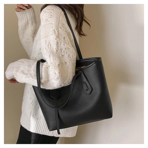 Close-up of black lychee grain leather tote bag worn with white knitted sweater