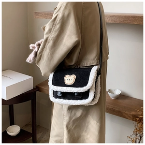 Détail de la bordure en fourrure et du patch ours sur un sac à bandoulière noir et blanc