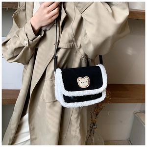 Détail d'un sac bandoulière en polaire noire avec écusson ours porté avec un trench