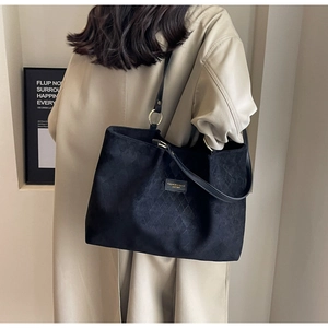 Detail of black quilted tote bag with gold hardware on a beige trench coat
