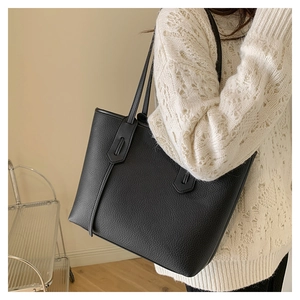 Detailed shot of lychee-textured leather tote bag with shield-shaped strap attachment