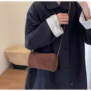 Close-up of a brown matte suede Boston cylinder bag worn by a model in a minimal setting