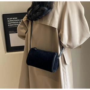 Minimalist black cylinder crossbody bag in matte suede shown on model's side back