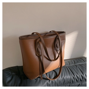 Detailed close-up of brown litchi grain leather tote bag with unique strap hole design